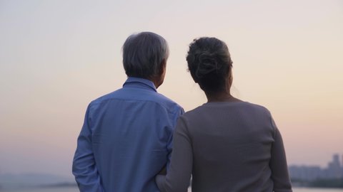 rear view of loving asian senior couple standing by a river looking at sunset