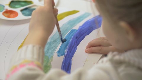 the left-handed girl draws a rainbow with watercolor paints and brushes, children's joint creativity.