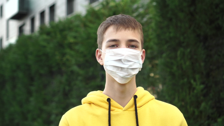 Young man teenager takes off a protective medical blue mask and laughs on a background of green vegetation. The idea of optimism and personal protective equipment against coronavirus and plant pollen  Royalty-Free Stock Footage #1046170552