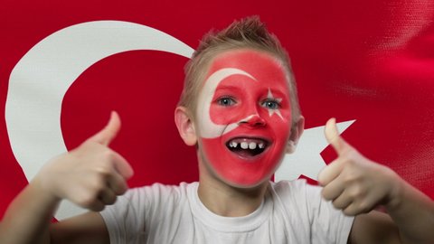 Turkish fan is celebrating. Boy with the country flag is watching the match. Football fan at the stadium is screaming. Soccer. Footballer with a painted face. Winner.
