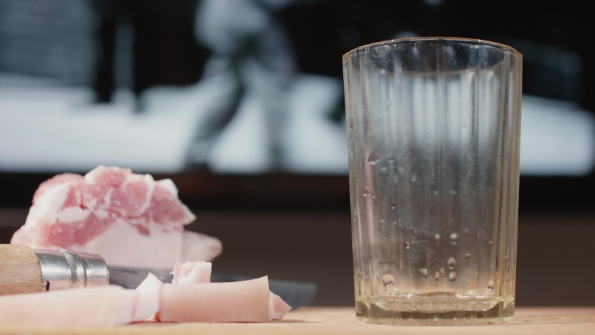 Alcohol abuser pours vodka into shotglass on wooden cutting board. Blurred black and white movie on background. Man's alcholism.