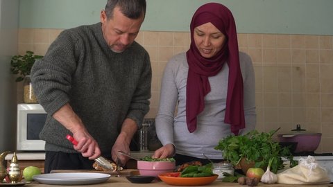 Middle-aged happy arabic couple together preparing food in a kitchen. Authentic muslim husband and wife cooking together at home. Slow Motion