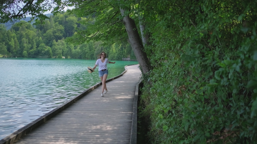 woman is running and whirling on coast of lake on nature in summertime, smiling