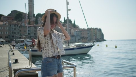 Happy girl in sunglasses spinning and posing with straw hat on waterfront of Rovinj, Croatia. Summer scene with Adriatic Sea