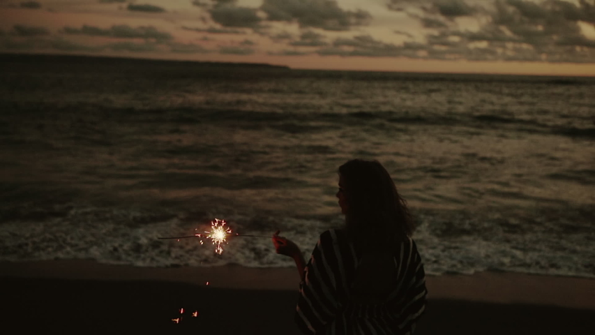 Close up portrait of young beautiful woman at sunset on the beach. Pretty girl celebrating new years eve and independence day or holiday with fireworks. City people travel. Business woman at vacation.