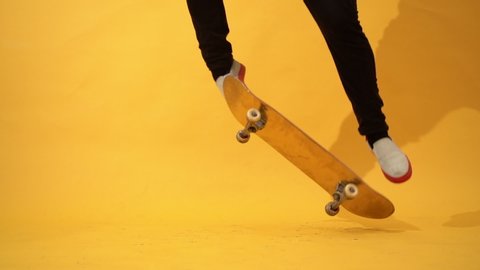 Skateboarder performing skateboard trick in the studio. Athlete practicing stunt jump on yellow background, preparing for competition. Extreme sport, youth culture
