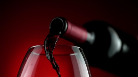 Super Slow Motion Detail Shot of Pouring Red Wine from Bottle on Luxury Red Gradient Background at 1000fps.