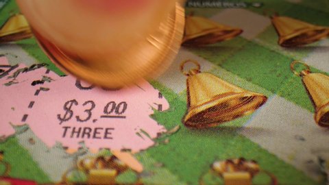 Close-up of using a lucky penny to scratch off an instant lottery ticket with bell symbols.

