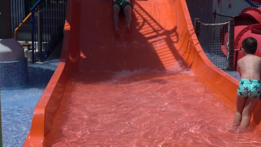 Father and son slide on slider in water park on summer holiday. Happy family on vacation. Slow motion 240 fps
