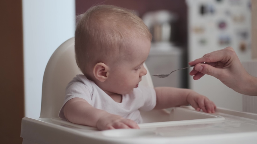 Cute little baby feeding with a spoon at the table, infant eating meal foods. 4k 50 fps Royalty-Free Stock Footage #1046230846