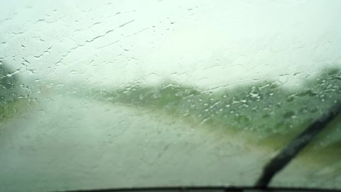 Rain drops on windshield and car wipers are removing water. Driving in rain view from inside car with rain drops on car windshield. Rain drops on window car windshield.Tanzania, Africa. Slow motion