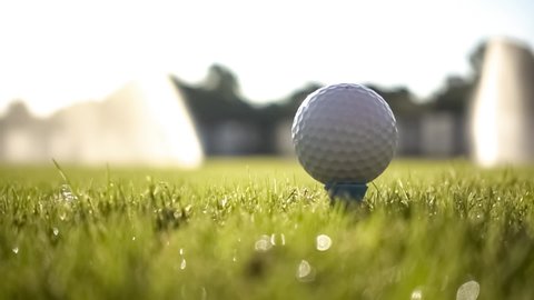 Golf club hits a golf ball in a super slow motion. Drops of morning dew and grass particles rise into the air after the impact.