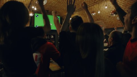MED FIXED Model released, fans watching a game on a large TV in a sport pub, celebrating a goal, green screen chroma key with tracking points. 4K UHD, shot on ARRI Alexa Mini with Cooke S4 lenses