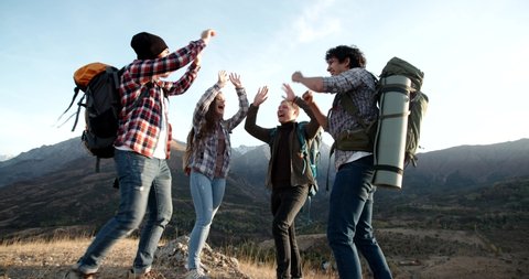 Students on hike adventure - Four young authentic people cheering on top of mountain, doing a highfive, expressing positive emotions - friendship, travel destination 4k footage