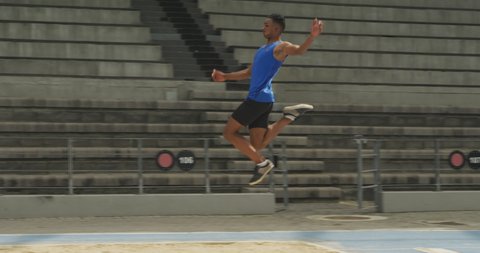 Side view of a mixed race male athlete practicing at a sports stadium, doing long jump, slow motion. Track and Field Sports Training in Stadium.