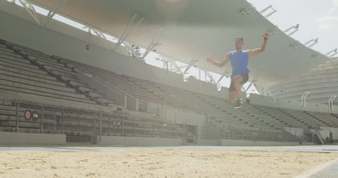 Front view of a mixed race male athlete practicing at a sports stadium, doing long jump, slow motion. Track and Field Sports Training in Stadium.