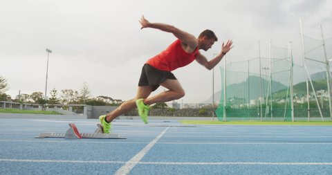 Side view of a Caucasian male athlete practicing at a sports stadium, starting sprinting from running blocks, slow motion. Track and Field Sports Training in Stadium.