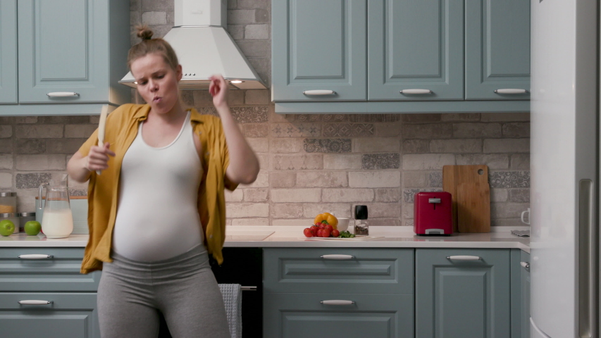 Pregnant Mom Listening Music and Relaxing Stay at Home. Portrait Carefree Smiling 30s Woman Standing in Kitchen Sunny Day. Concept Pregnancy and Holidays. Cute Fun Mum Dancing and Preparing Party 4K | Shutterstock HD Video #1046244751