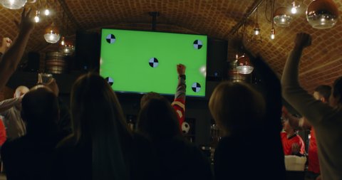 HANDHELD Model released, fans watching a game on a large TV in a sport pub, goal celebration, green screen chroma key with tracking points. Shot on ARRI Alexa Mini with Atlas Orion 2x Anamorphic lens