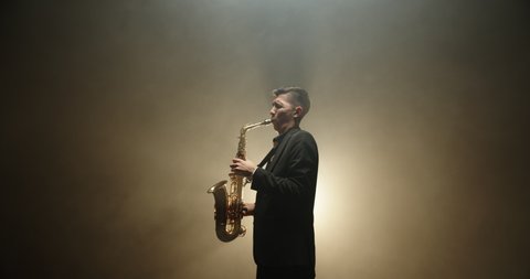 Cool caucasian saxophone player performing a solo on smoked stage, spotterd by light - the arts, jazz concept 4k footage