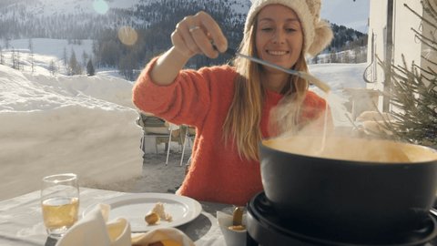 Happy young woman eating cheese fondue in Switzerland enjoying the Alps and snowcapped mountains in winter season holidays. People food tradition local concept 