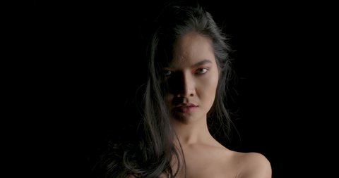 Close up Portrait shot of sexy asian woman giving a tempting look in low key light on black background. 