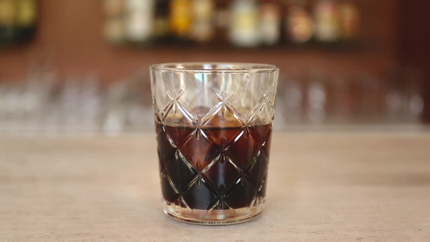 Glass of tasty alcoholic Black and white russian cocktail with vodka and coffee liquor on bar stand, making of a cocktail | Shutterstock HD Video #1046260237