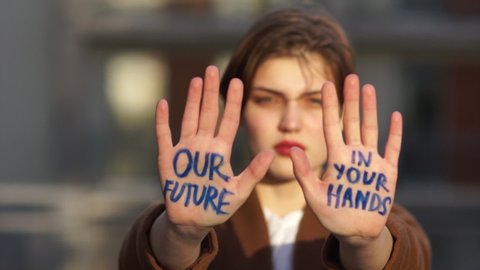 Climat strike, environmental disaster. Close portrait of a beautiful student with an inscription on the palms. Our future in your hands. Young woman protests against global warming