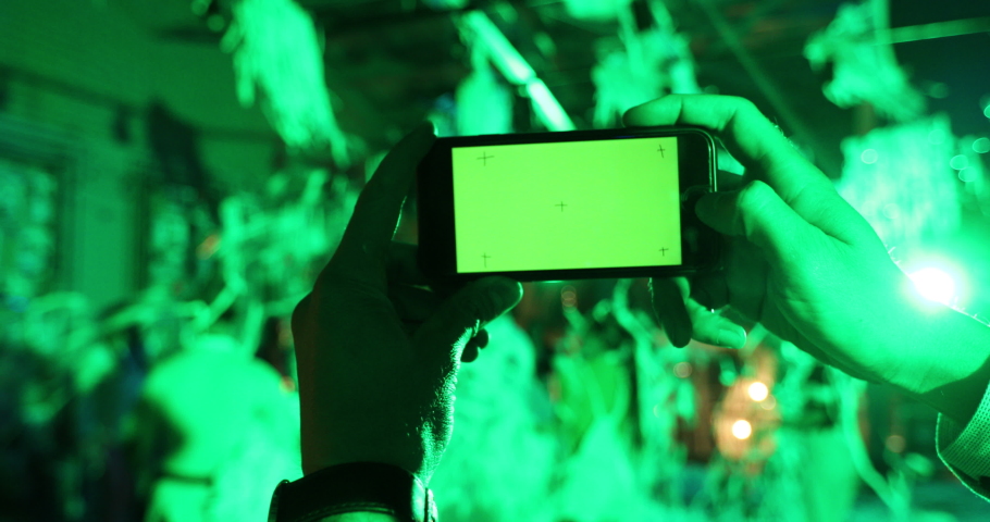 Close up male hand holding a black mobile phone with a chroma key green screen, party with paper tinsel background