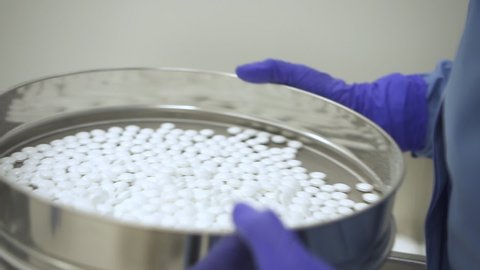Closeup of a scientist hand holding and showing some white pills in a laboratory. quality control concept. Pharmacology expert checking tablets. pharmaceutical factory plant.