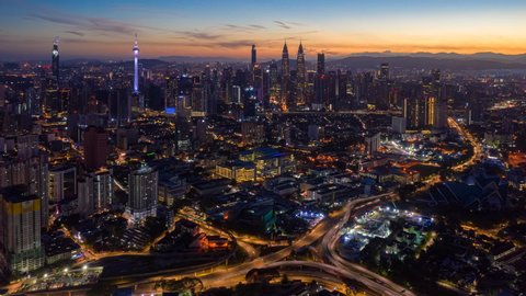 Time lapse: Aerial city view during dawn overlooking Kuala Lumpur city skyline from afar with busy roundabout and streets.