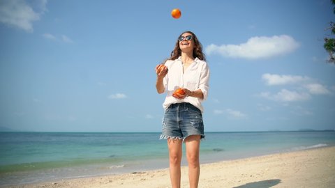 Young cheerful woman juggles tangerines on the beach on a sunny day. Having fun on the vacation.