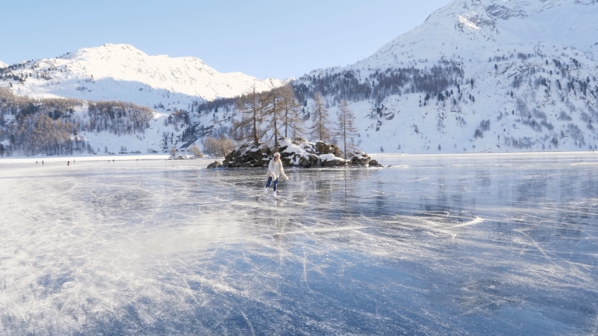 Young woman ice skating on frozen lake in winter. Female on ice skates surrounded by stunning mountain landscape. Natural frozen lake in the Alps. Woman enjoying winter season 