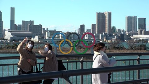 TOKYO, JAPAN - MAR 2020 : The five ring symbol of the Olympic Games at Odaiba. Tokyo Olympic 2020 has been postponed to 2021 due to novel coronavirus pandemic. People wearing surgical masks.