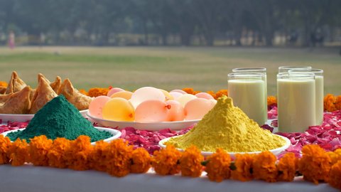 Pan shot of a beautifully decorated festive table for Holi festival celebrated in India. Heaps of colorful Gulal with plates of samosas, Indian sweet Gujiyas, Kesar Thandai, and water bombs on the ...