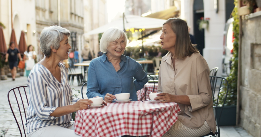 Three Caucasian senior women friendly chatting and drinking coffee at table in cafe terrace in summer. Female friends talking and laughing outdoor while gossiping and sipping tea. | Shutterstock HD Video #1046309653