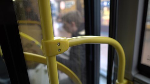 The bus pulls up to the stop, the glass doors open and a person enters the cabin. View from inside the bus. Faceless. Close-up of the yellow handrail. Blurred background. Abstraction. 4K.