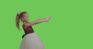 Kid wearing ball dress like princess pointing to side and upwards showing object in copy space over green screen background. Girl having fun on Chroma Key. 4k raw video footage slow motion 60 fps