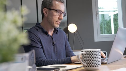 Middle-aged guy having hot drink, working on laptop