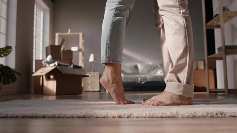 Close-up low angle shot of legs of a cute couple walking barefoot on floor of their new home. Girl standing on tip-toes to kiss her boyfriend - love, new life concept 4k footage