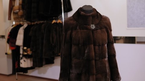 Beautiful mink coat on a mannequin in a women's clothing store. Slow motion. Fur products store. Many different coats of different fur on hangers in the clothing store.