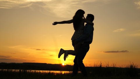 Young couple dancing at sunset on beach. Happy guy and girl waltz in evening in summer park. Loving man and woman dance in bright rays of sun on the background of the lake.