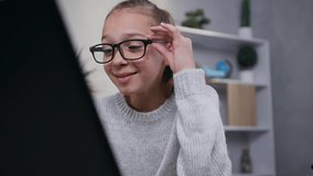 Close view of cheerful modern 15- year old schoolgirl in eyeglasses laughing from amusing video on computer monitor at home