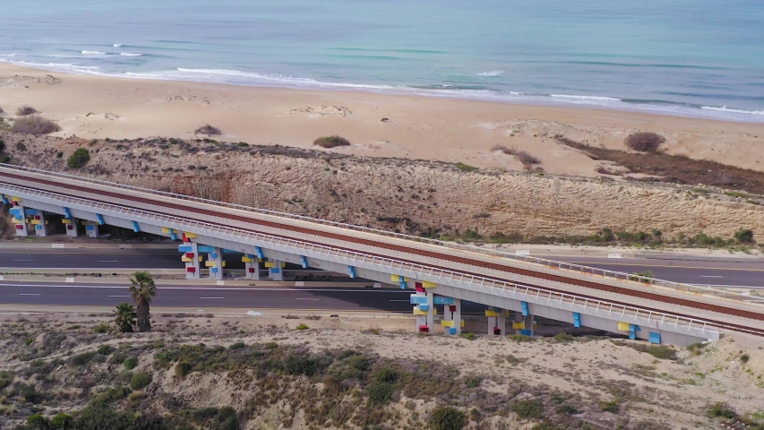 Traffic on a coastal highway, with sandy beach in the distance, aerial view.