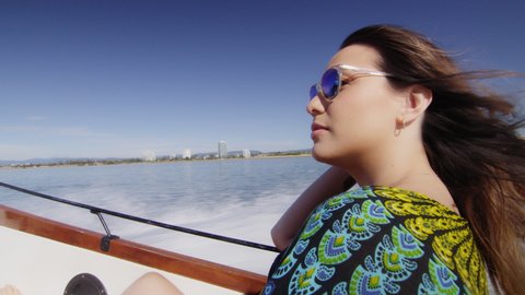 Handsome young man driving a wooden motorboat and beautiful young woman wearing sunglasses in the back, under a sunny blue sky. Close to long shot on 4K RED camera.