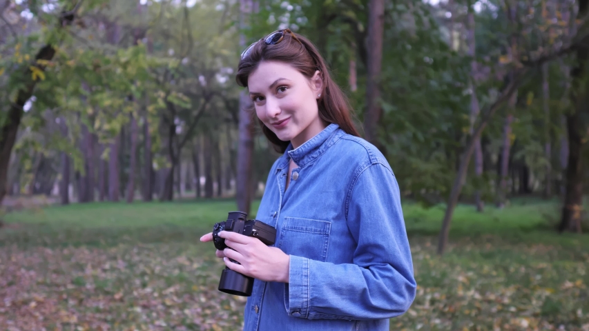 Portrait of a professional freelancer with a camera in hand in the autumn forest at sunset. The girl smiles and looks into the camera, a wide static shot