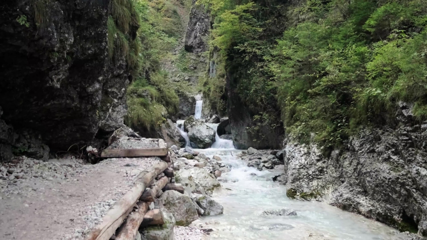 A man exploring Martuljek Waterfall during the day in Gozd Martljek in Slovenia and the Triglav National Park. Man walking with cliffs next to him and river running below