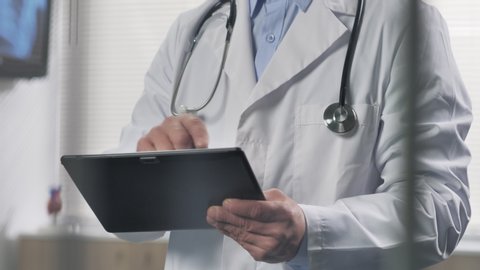doctor standing uses tablet computer behind a glass close up on hands half bust