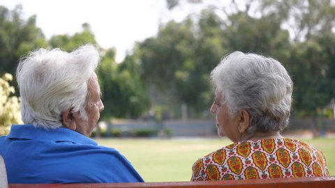 Back view shot of an old couple spending quality time together - couples lifestyle. Senior white-haired male and female hugging each other while sitting together on a bench in a park - happy relati...