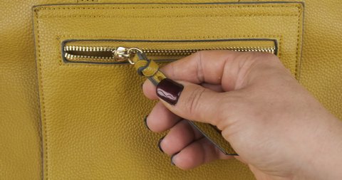 Hand opens the lock with a zipper, a pocket of a yellow women bag. Close-up.